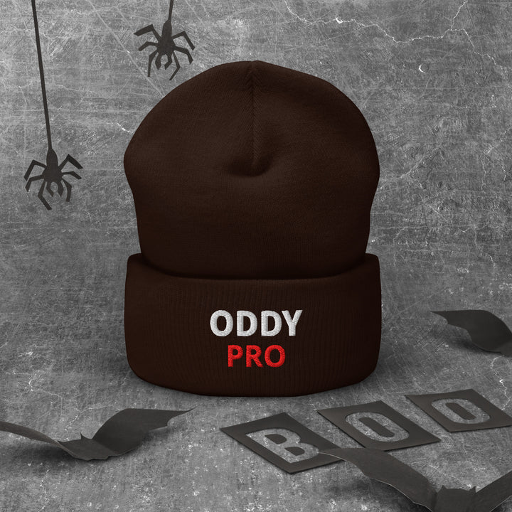 Oddy Pro Cuffed Beanie in brown with bold text, lying on a textured background with Halloween decorations.